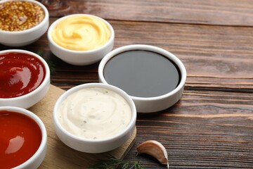 Different sauces in bowls on wooden table, closeup