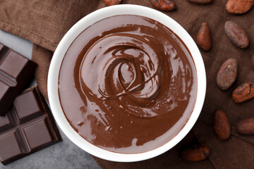 Bowl with melted chocolate, beans and pieces on grey table, flat lay