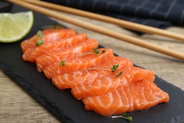 Fresh salmon sashimi with microgreens and lime on wooden table, closeup