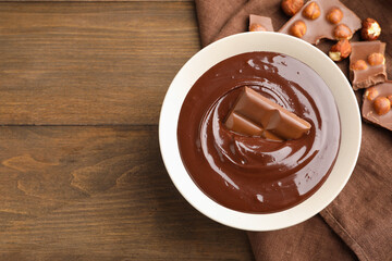 Melted chocolate and pieces with hazelnuts on wooden table, flat lay. Space for text