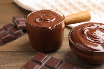 Melted chocolate and pieces on wooden table, closeup