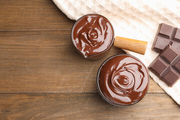 Melted chocolate and pieces on wooden table, flat lay. Space for text