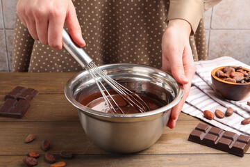 Woman mixing melted chocolate in bowl at wooden table, closeup
