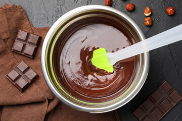 Melted chocolate and pieces with hazelnuts on black table, flat lay