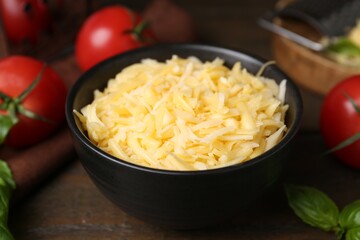 Grated cheese in bowl, tomatoes and basil on wooden table, closeup