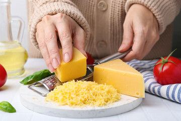Woman grating cheese at white tiled table, closeup