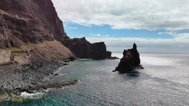 Aerial drone flight towards the monumental Roque de La Bonanza rock formation, standing isolated in the Atlantic Ocean off the volcanic coast of El Hierro, Canary Islands, Spain.