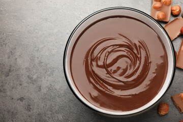 Melted chocolate in bowl and pieces with nuts on grey table, flat lay. Space for text