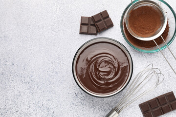 Melted chocolate in bowl, pieces, cocoa powder and whisk on light grey table, flat lay. Space for text