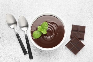 Melted chocolate with mint in bowl, pieces and spoons on light grey table, flat lay
