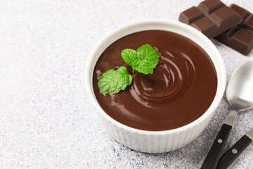 Melted chocolate with mint in bowl, pieces and spoon on light grey table, closeup. Space for text