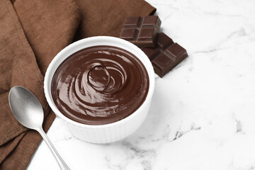 Melted chocolate in bowl, pieces and spoon on white marble table, closeup. Space for text