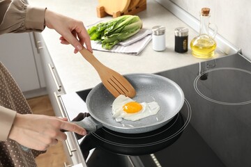 Woman taking fried egg with slotted spatula in kitchen, closeup