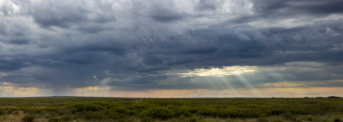 panorama of thick dark rainy clouds pierced by a ray of sunshine
