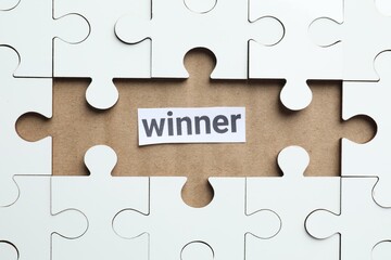Fototapeta premium Paper note with word Winner and jigsaw puzzle pieces on carton, top view