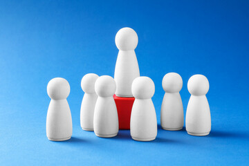 Winner. Human figures, wooden one on red cube against light blue background