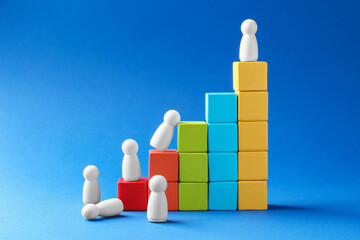Winner. Human figures, wooden one on top of stacked cubes against light blue background