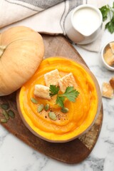 Tasty pumpkin cream soup with seeds, parsley and croutons served in pumpkin on white marble table, flat lay