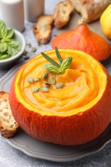 Tasty pumpkin cream soup with seeds and basil served in pumpkin on grey table, closeup
