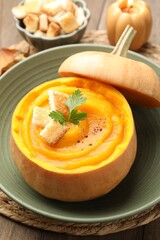 Tasty pumpkin cream soup with parsley and croutons served in pumpkin on wooden table, closeup