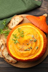 Tasty pumpkin cream soup with parsley and seeds served in pumpkin on wooden table, top view