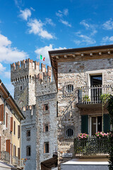 Picturesque streets of Sirmione, enjoying views of a historic Scaligero Castle and vibrant buildings under a clear blue sky by Lake Garda. Sirmione, Lombardy, Italy