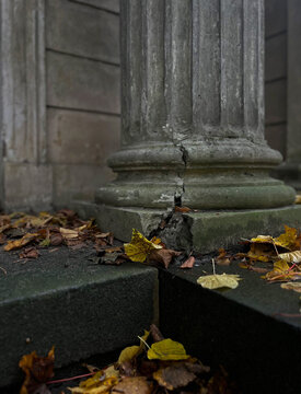 Old cracked stone column base with autumn leaves on the ground. Weathered architecture detail of ancient pillar with moss and decay, symbol of time and impermanence.