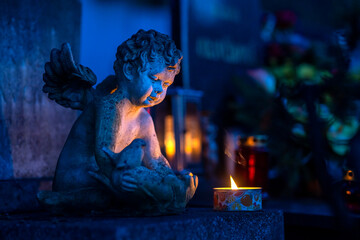 Statue of an angel in a cemetery at night with a burning candle.Memory of the deceased. Expression...
