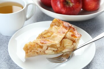 Piece of delicious homemade apple pie, fork and tea on grey textured table, closeup