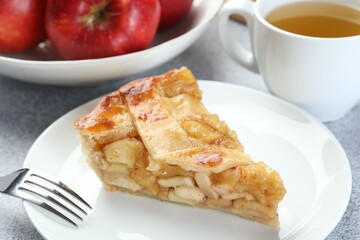 Piece of delicious homemade apple pie, fork and tea on grey textured table, closeup