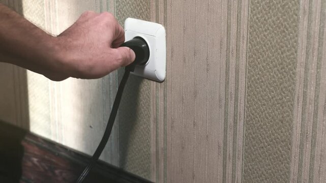 Male hand unplugging plug into wall socket. Close-up power socket