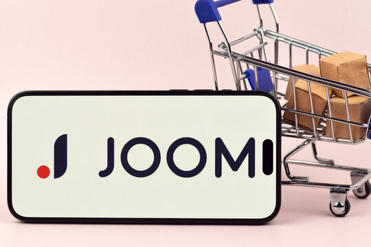 The shopping cart with a smartphone there is Joom open on the screen on white background.