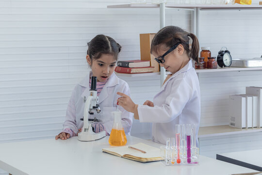 Elementary pupils in white gowns studying a chemical experiment in laboratory, kids in chemistry class using pipette dropping liquid to test tube, student workshop training in science classroom - Powered by Adobe
