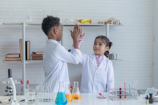 Happy children in gown uniform doing science experiments in classroom together with friends. Science education in laboratory lab with elementary diversity students in class.