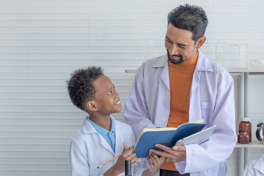 Adorable African American boy school student wearing lab coats happy studying with Indian teacher sending experiment paperwork in laboratory room, lifestyle learning education science class for kid - Powered by Adobe