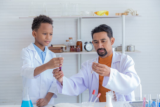 Cheerful African boy primary school students wearing lab coats studying with Indian teacher attention to chemical substance in test tube in laboratory room, lifestyle learning education science class