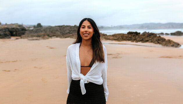 Portrait of confident woman smiling on the beach with rocky background