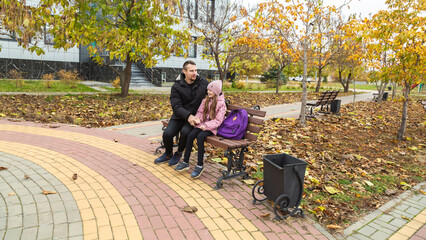 Father meets child from school. Dad with daughter sitting on beanch