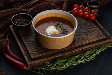 Solyanka soup in disposable bowl on a wooden tray