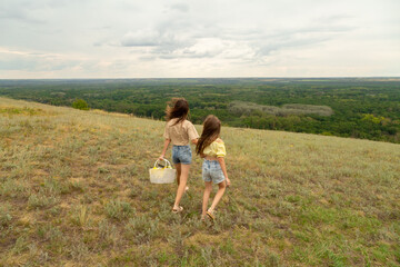 Fototapeta premium Family on a meadow, mother and daughter holding hands while carries picnic basket