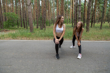 Obraz premium Mother and little daughter are doing exercise in the forest.
