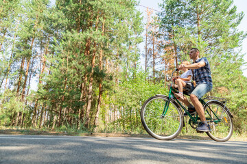 Naklejka premium A young father carries his little daughter in a bicycle seat. Dad and child ride a bike in forest