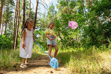 Fototapeta premium Two little girls catching insects with nets in forest