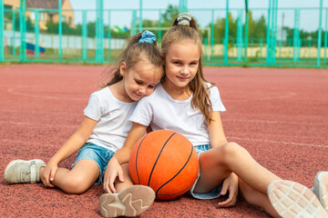 Cheerful little laughing kids is sitting at the stadium holding a basketball. Children play ball on the playground