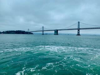 A striking view of a suspension bridge spanning over calm blue-green waters under a cloudy sky