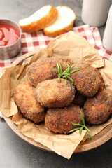 Delicious patties with rosemary in bowl on grey textured table, closeup