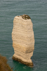 Lone white limestone rock formation rising from turquoise sea near Étretat, Normandy. Peaceful coastal scene showcasing the beauty of erosion and marine nature.