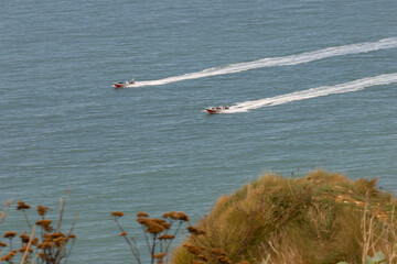 Two motorboats speeding across the calm blue sea near the cliffs of Étretat, Normandy. A dynamic coastal scene blending motion and natural beauty.