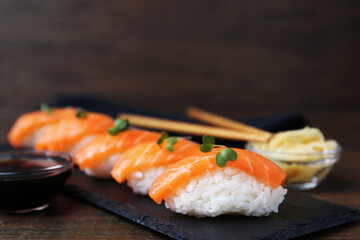 Delicious nigiri sushi with salmon, microgreens and soy sauce on wooden table, closeup
