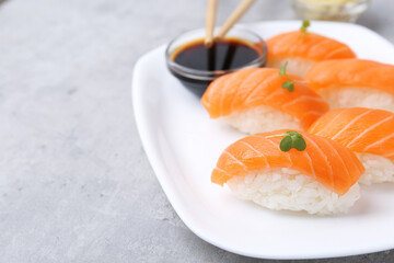 Delicious nigiri sushi with salmon, microgreens and soy sauce on grey textured table, closeup. Space for text